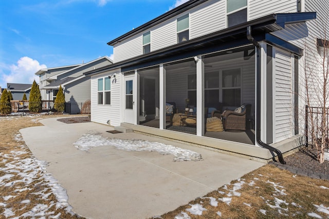 snow covered rear of property with a patio, fence, and a sunroom