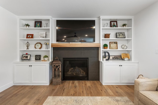 living room with light wood-type flooring, built in shelves, and a glass covered fireplace