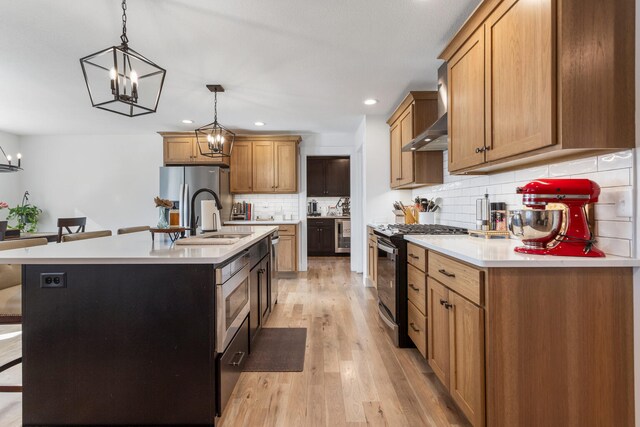 kitchen featuring gas stove, light countertops, a center island with sink, and stainless steel refrigerator with ice dispenser