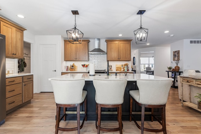 kitchen with visible vents, an island with sink, open floor plan, light countertops, and wall chimney range hood