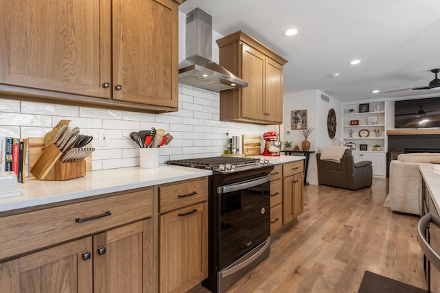 kitchen with island range hood, light wood-style flooring, open floor plan, stainless steel gas range, and light countertops