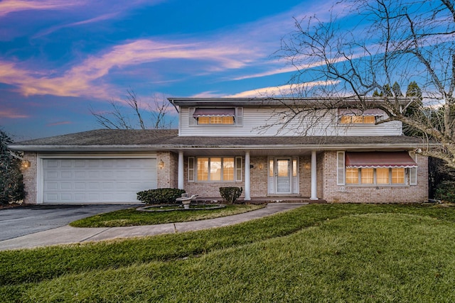 traditional-style home with an attached garage, aphalt driveway, a lawn, and brick siding