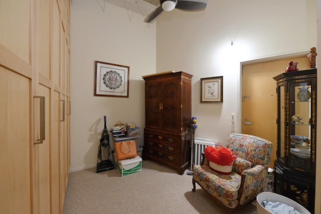 living area featuring light carpet, ceiling fan, and a high ceiling