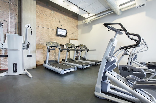 gym featuring a high ceiling and brick wall