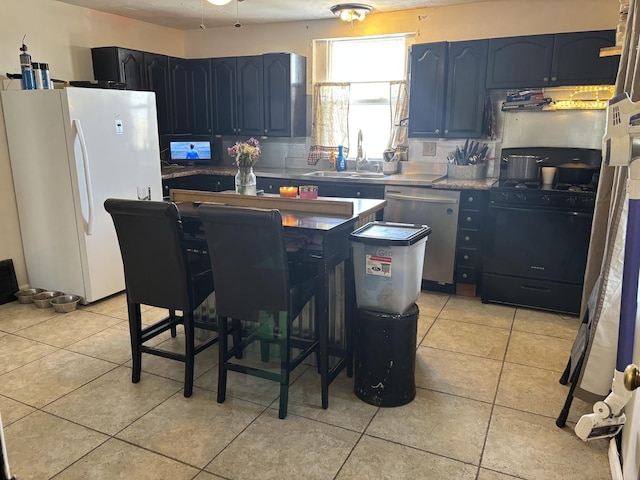 kitchen with blue cabinetry, black gas range oven, stainless steel dishwasher, freestanding refrigerator, and a sink