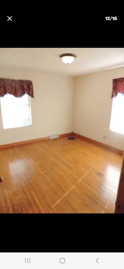 empty room with baseboards, visible vents, and wood finished floors