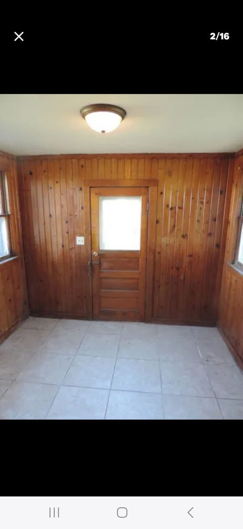 doorway with wood walls and light tile patterned flooring