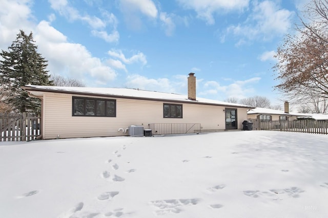 snow covered property with central AC unit, a chimney, and fence