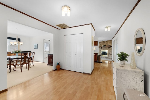 foyer featuring a fireplace, crown molding, visible vents, and light wood finished floors