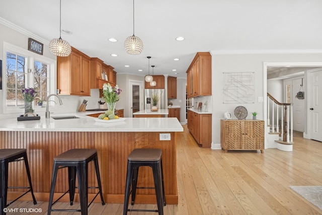 kitchen featuring a peninsula, a sink, light countertops, hanging light fixtures, and stainless steel fridge with ice dispenser