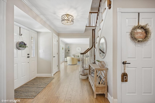 entryway featuring light wood finished floors, baseboards, stairway, and crown molding