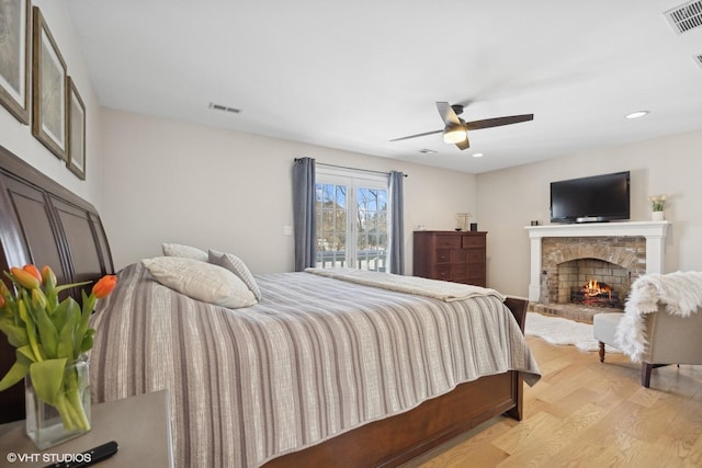 bedroom featuring visible vents, ceiling fan, a stone fireplace, and light wood finished floors