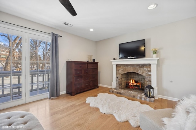 living area with light wood-style floors, visible vents, a stone fireplace, and baseboards