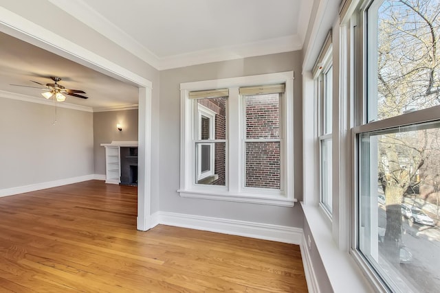 unfurnished sunroom featuring ceiling fan, ornamental molding, and light hardwood / wood-style flooring