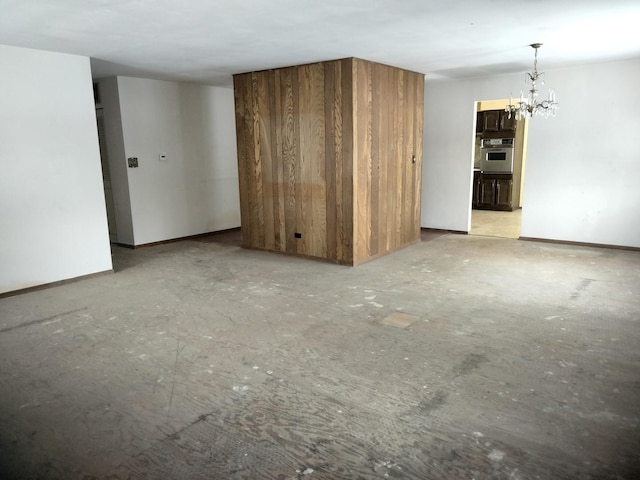 unfurnished living room featuring an inviting chandelier and baseboards