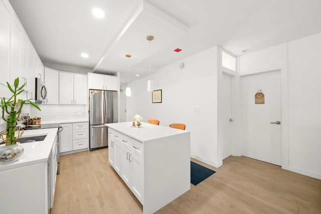 kitchen with a center island, light wood-type flooring, appliances with stainless steel finishes, pendant lighting, and white cabinets