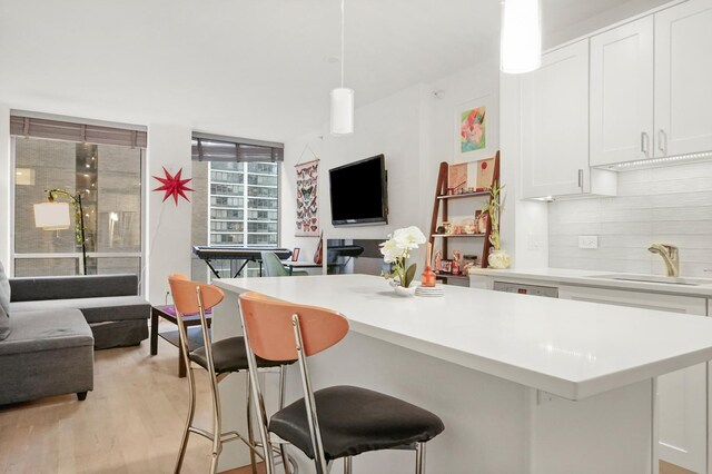 kitchen featuring pendant lighting, white cabinetry, sink, backsplash, and a kitchen bar