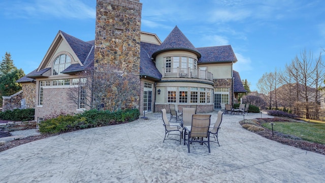 rear view of property with stucco siding, french doors, a chimney, a balcony, and a patio area