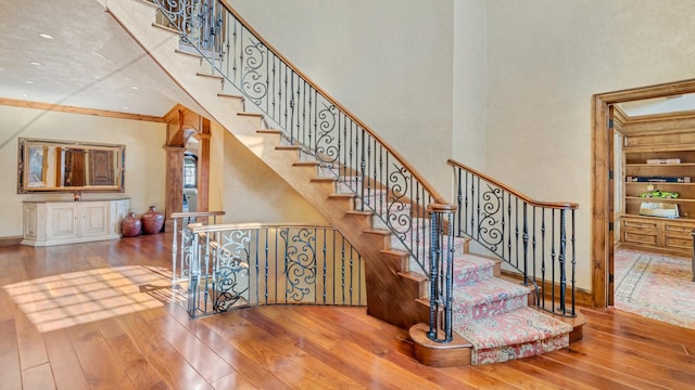 stairway with hardwood / wood-style flooring, built in features, a high ceiling, crown molding, and baseboards