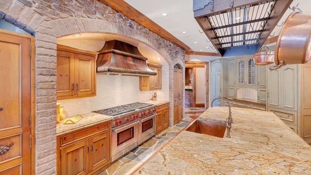 kitchen featuring a sink, tasteful backsplash, stone tile floors, range with two ovens, and custom exhaust hood