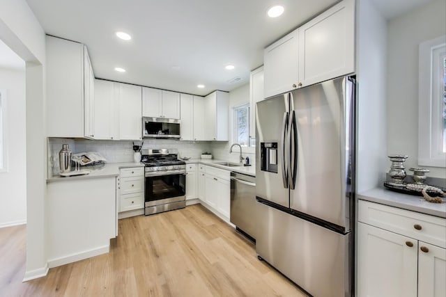 kitchen with decorative backsplash, stainless steel appliances, light countertops, white cabinetry, and a sink