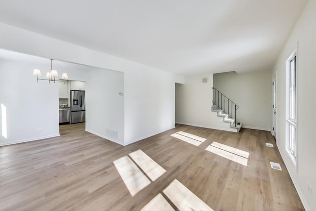 unfurnished living room with light wood-style floors, visible vents, stairway, and an inviting chandelier