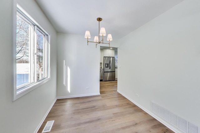 unfurnished dining area featuring light wood-type flooring, an inviting chandelier, baseboards, and visible vents