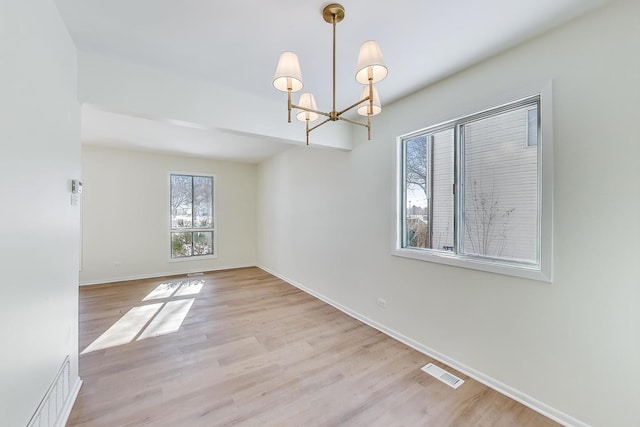 spare room featuring light wood-style floors, baseboards, visible vents, and a notable chandelier