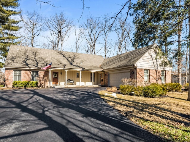 view of front of house featuring a garage, covered porch, aphalt driveway, and brick siding