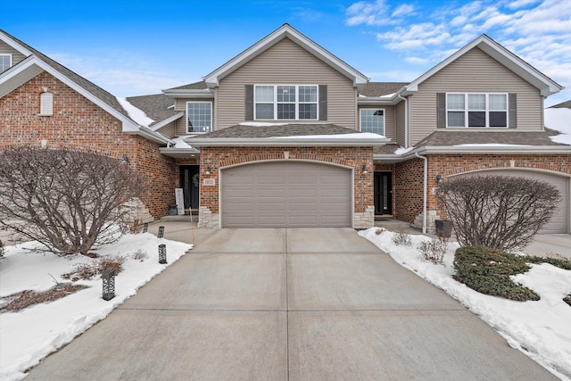 traditional-style home with a garage, roof with shingles, concrete driveway, and brick siding