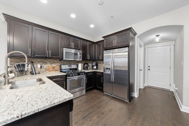 kitchen featuring light stone counters, stainless steel appliances, a sink, dark brown cabinets, and dark wood-style floors