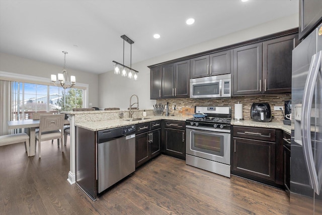 kitchen featuring a peninsula, appliances with stainless steel finishes, a sink, and decorative light fixtures