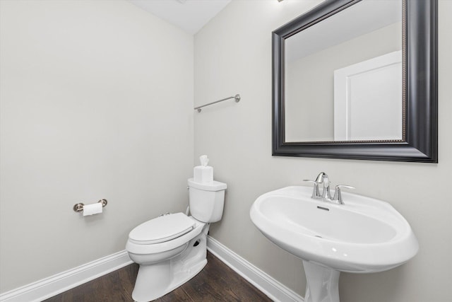 half bath with a sink, toilet, baseboards, and wood finished floors