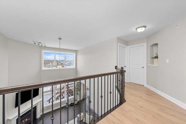 hall featuring track lighting, wood finished floors, an upstairs landing, and baseboards