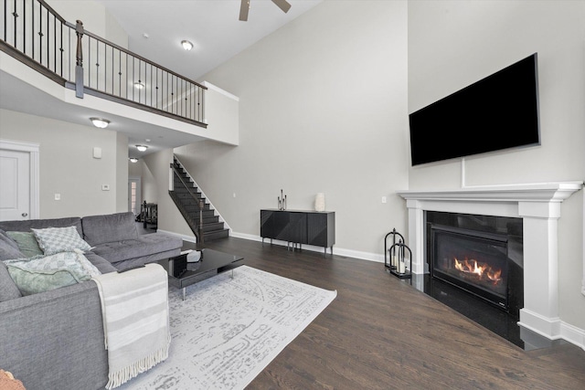 living area featuring dark wood-type flooring, a glass covered fireplace, stairway, and baseboards