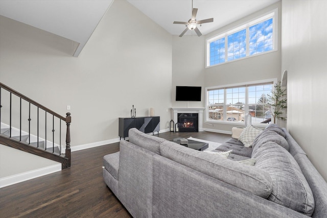 living room featuring baseboards, a glass covered fireplace, stairway, dark wood-style flooring, and a high ceiling