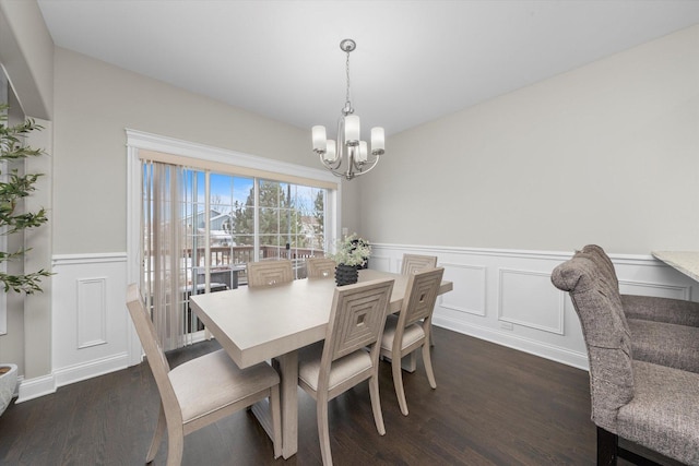 dining room with dark wood-type flooring, a decorative wall, wainscoting, and an inviting chandelier