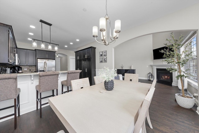 dining room with arched walkways, a warm lit fireplace, dark wood finished floors, and an inviting chandelier