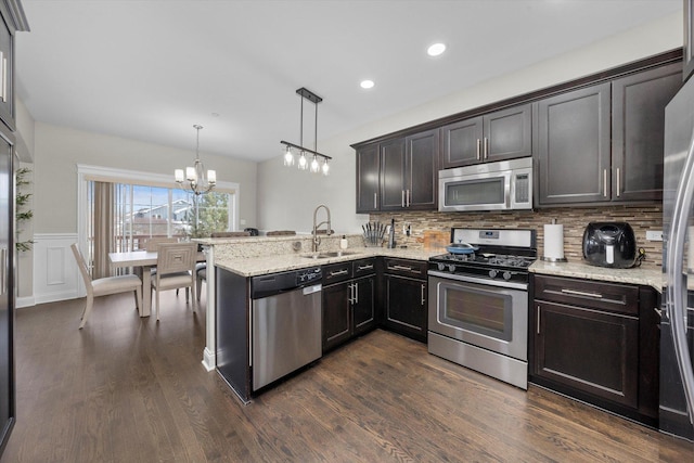 kitchen featuring decorative light fixtures, decorative backsplash, appliances with stainless steel finishes, a sink, and a peninsula