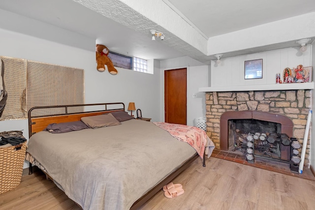 bedroom with light wood-style floors and a stone fireplace