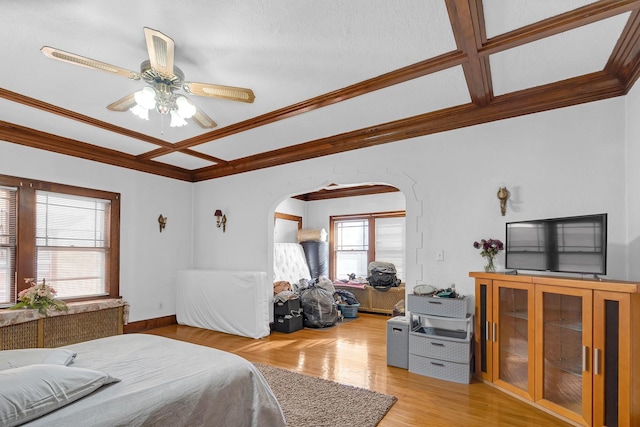 bedroom with arched walkways, coffered ceiling, radiator, ornamental molding, and light wood-style floors