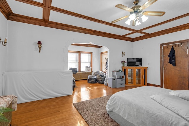 bedroom with arched walkways, coffered ceiling, ceiling fan, ornamental molding, and wood finished floors