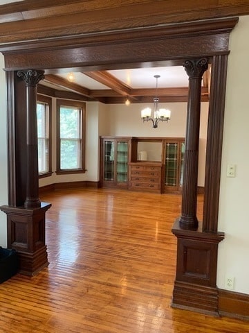 unfurnished living room featuring decorative columns, light wood-type flooring, beam ceiling, coffered ceiling, and a chandelier