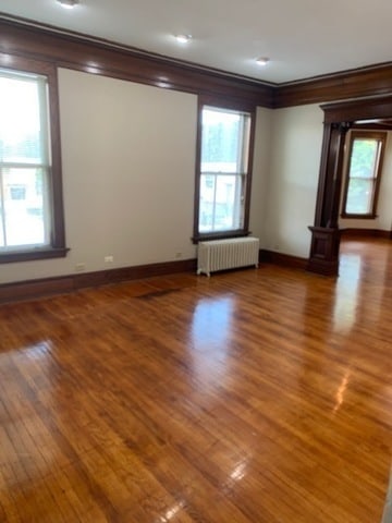 empty room featuring ornamental molding, wood-type flooring, and radiator heating unit