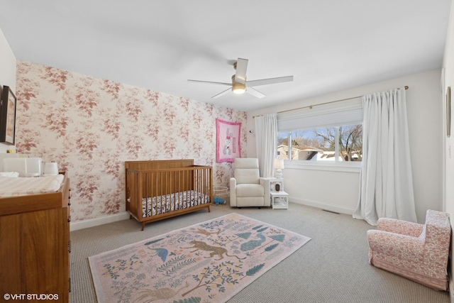 bedroom with light carpet, wallpapered walls, a crib, visible vents, and baseboards