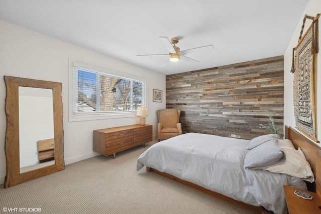 bedroom featuring light carpet, baseboards, ceiling fan, an accent wall, and wood walls