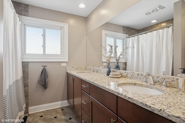 bathroom featuring double vanity, tile patterned flooring, a sink, and baseboards