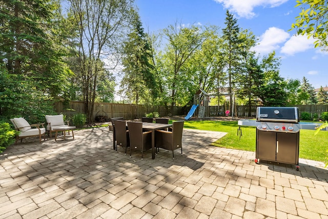 view of patio with area for grilling, outdoor dining space, a playground, and a fenced backyard