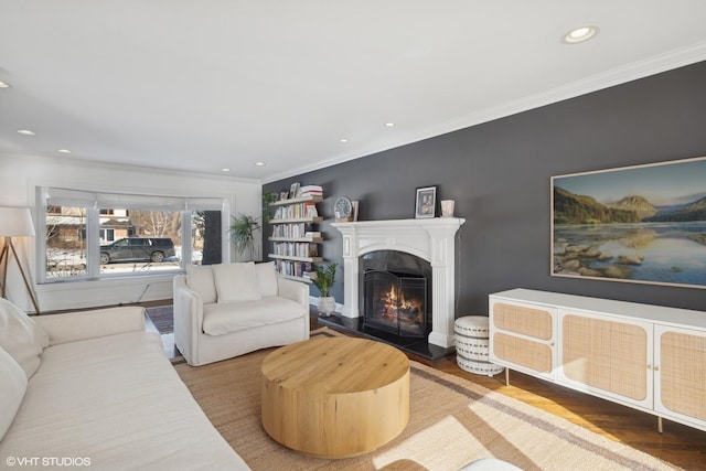 living room featuring a warm lit fireplace, recessed lighting, wood finished floors, and crown molding