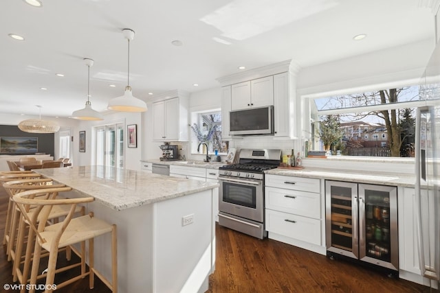 kitchen with light stone counters, wine cooler, a center island, appliances with stainless steel finishes, and white cabinets